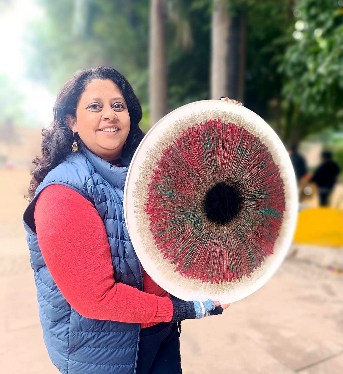 Piyusha Vir, the artist behind Resinaria, smiling outdoors as she holds her round red Iris resin artwork