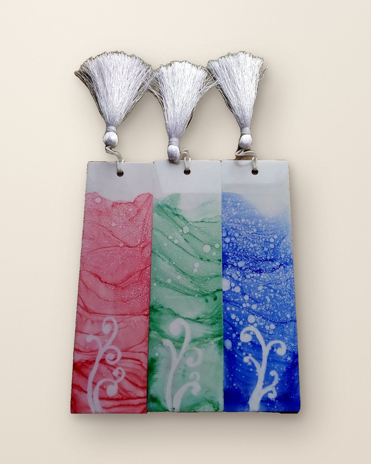 Three resin bookmarks in red, green and blue alcohol ink with white tassels
