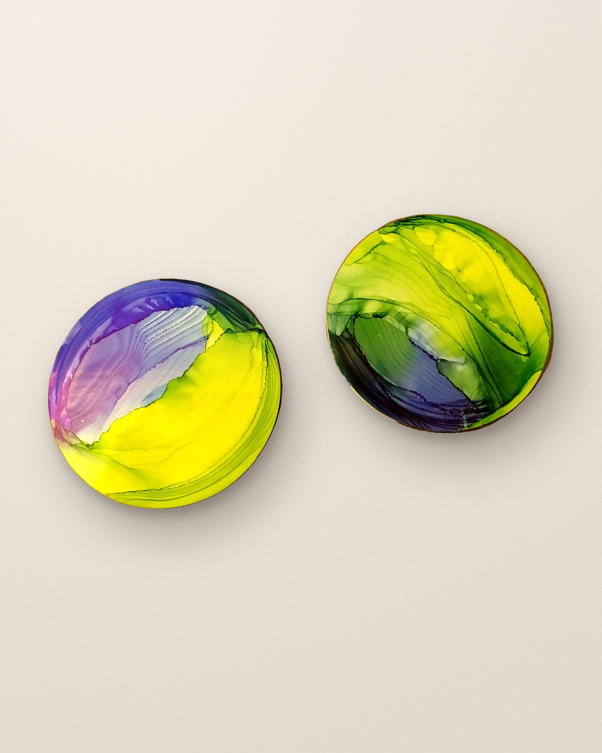 Two round alcohol ink resin coasters in violet, lime and yellow