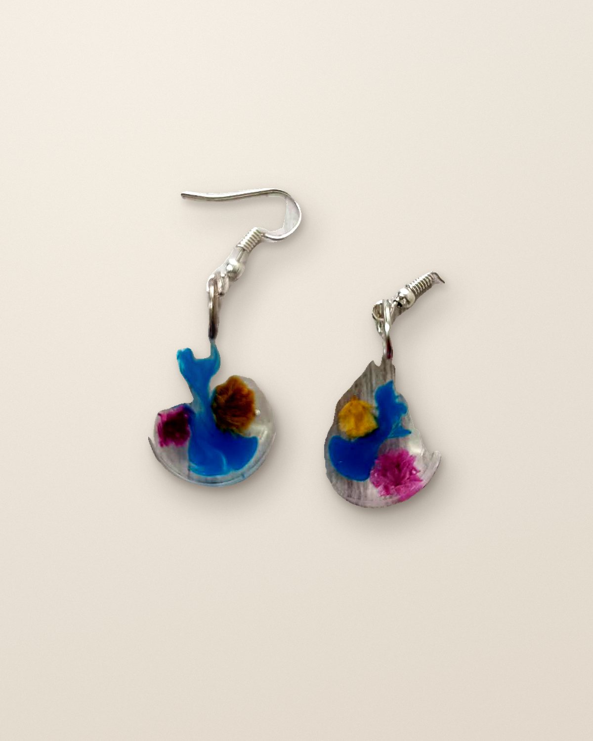 Clear teardrop resin earrings holding blue pigment and tiny pressed flowers