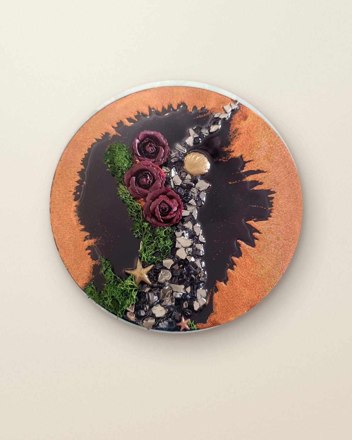 River of Hope, a round handcrafted resin artwork in copper and black with deep red roses, green moss and crystals, hung on a plaster wall